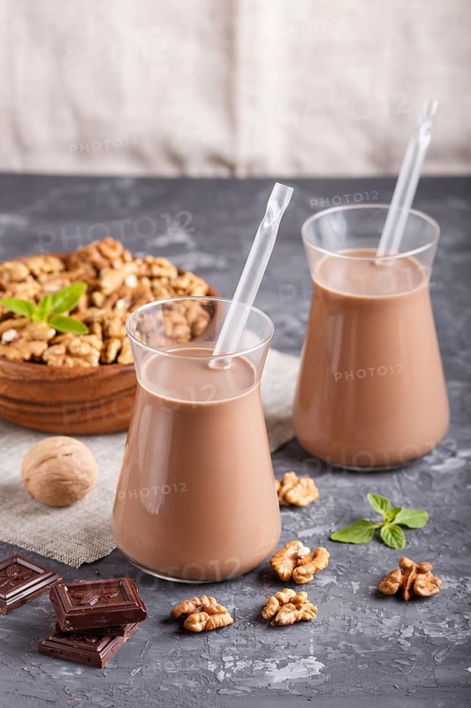 Organic non dairy walnut chocolate milk in glass and wooden plate with walnuts on a black concrete background. Vegan healthy food concept, close up, side view
