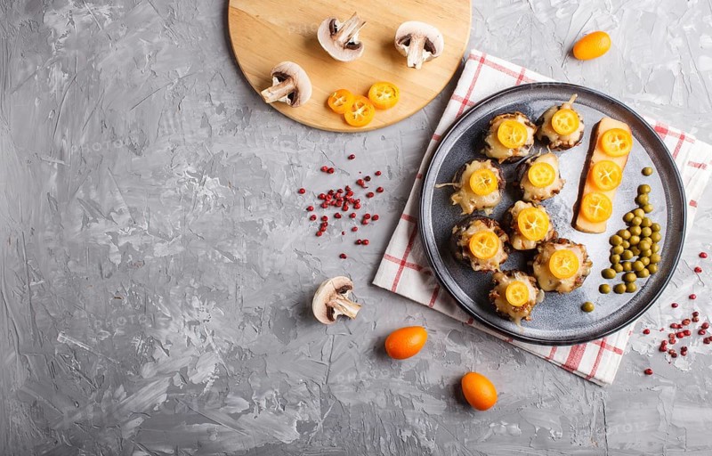 Stuffed fried champignons with cheese, kumquats and green peas on a gray concrete background. ceramic plate, top view, flat lay, copy space, horizontal