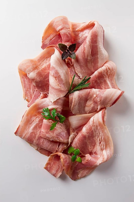 Raw bacon, sliced, with micro greenery and spices, on a white background, close-up
