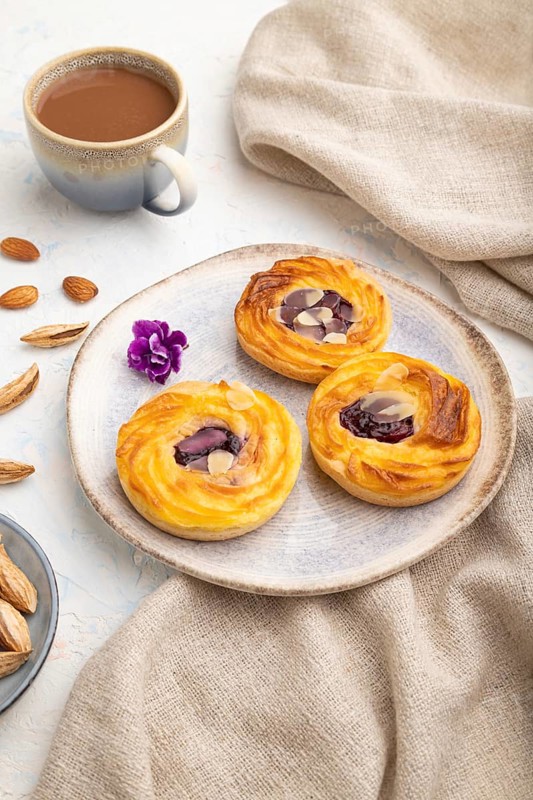 Small cheesecakes with jam and almonds with cup of coffee on a white concrete background and linen textile. Side view, close up