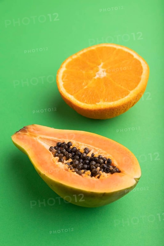 Ripe cut papaya and orange on green pastel background. Side view, close up. Tropical, healthy food, women health concept, minimalism