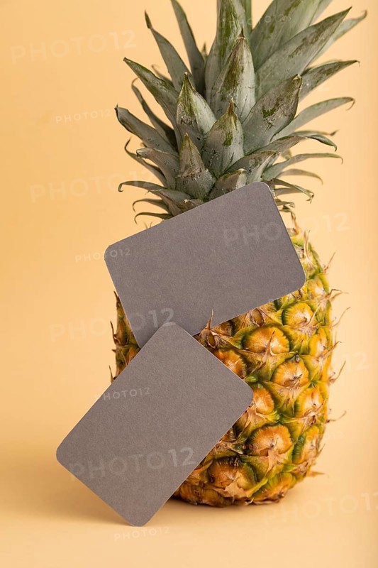 Gray paper business card with ripe pineapple on orange pastel background. Side view, copy space. Tropical, healthy food, vacation, holidays concept
