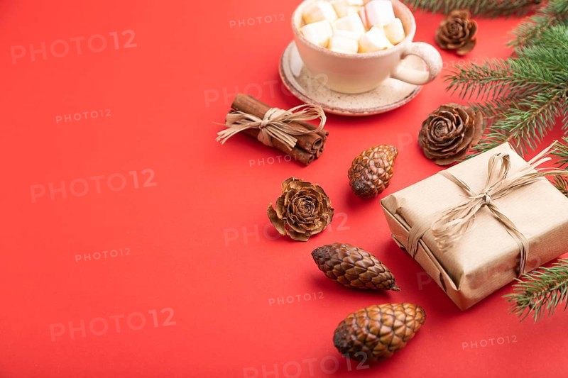 Christmas or New Year composition. Decorations, box, cinnamon, cones, fir and spruce branches, cup of coffee, on a red paper background. Side view, copy space