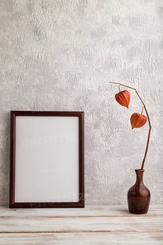Brown wooden frame mockup with physalis in ceramic vase on gray concrete background. Blank, vertical orientation, still life, copy space