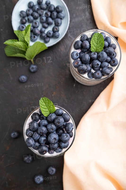 Yogurt with blueberry and chia in glass on black concrete background and orange linen textile. top view, flat lay, close up