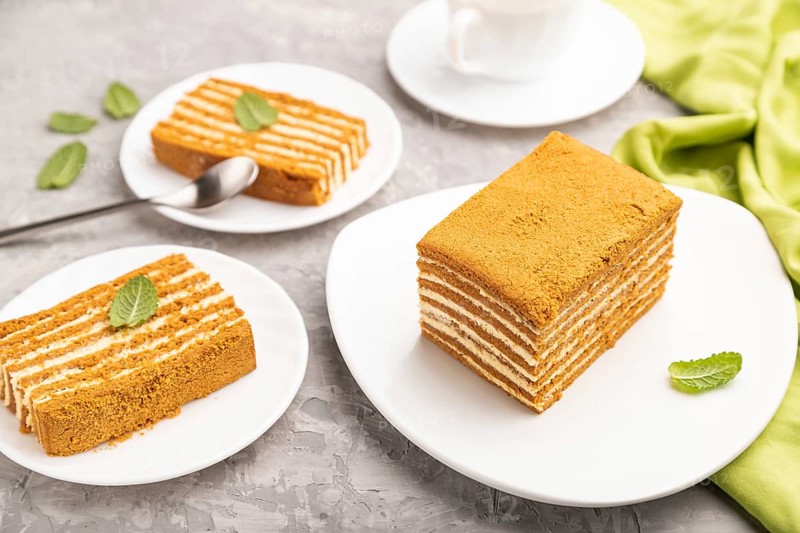 Homemade honey cake with milk cream and mint with cup of coffee on a gray concrete background and green textile. Side view, close up, selective focus