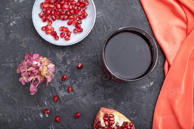 Glass of pomegranate juice on a black concrete background with red textile. Top view, close up, flat lay