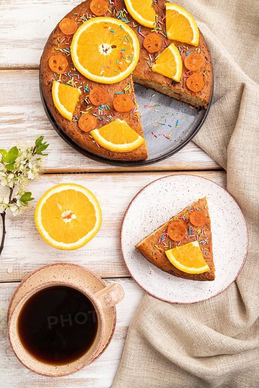 Orange cake and a cup of coffee on a white wooden background and linen textile. Top view, flat lay, close up