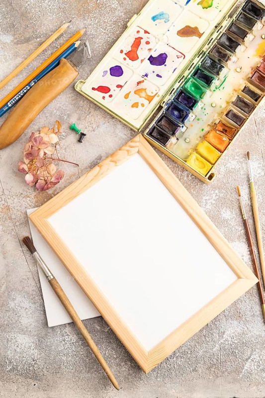 Drawing accessories set: brushes, pencils, watercolor, frame on brown concrete background. Top view, flat lay