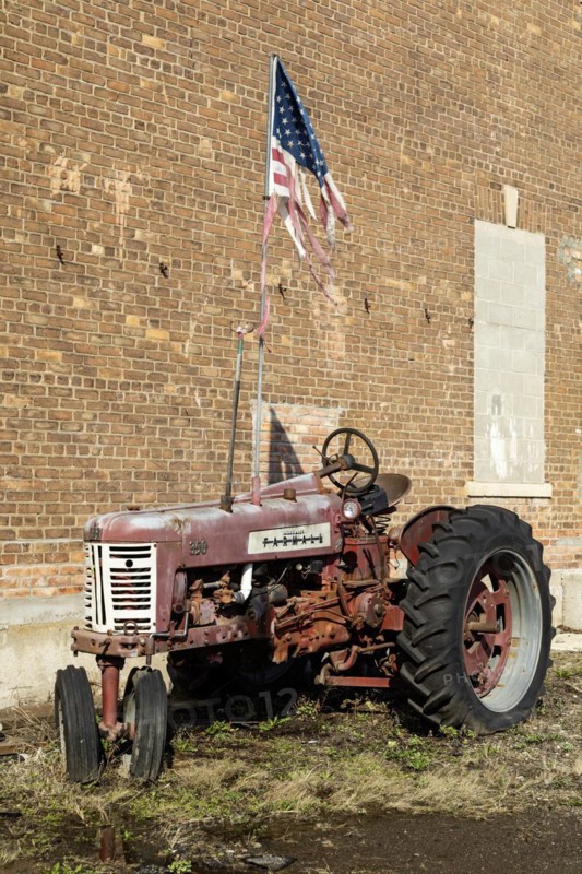 Detroit, Michigan, An old McCormick Farmall tractor flies a tattered American flag outside an auto repair shop