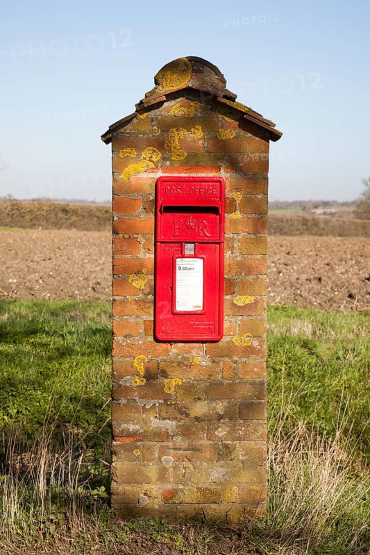 Scarlet red Post Office pillar box mounted in brick with fields in background, Hoo, Suffolk, England, United Kingdom, Europe
