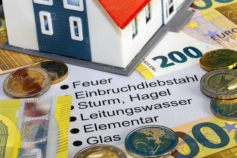 Symbolic image of building insurance: close-up of contract documents, a model house, euro banknotes and euro coins