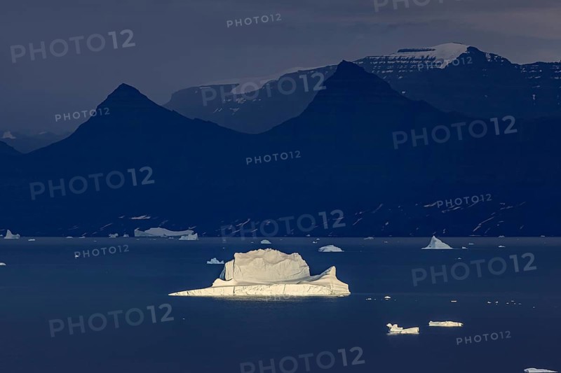 Evening light on an iceberg in a fjord in front of steep mountains, cloudy, autumn, Scoresby Sund, East Greenland, Greenland, North America