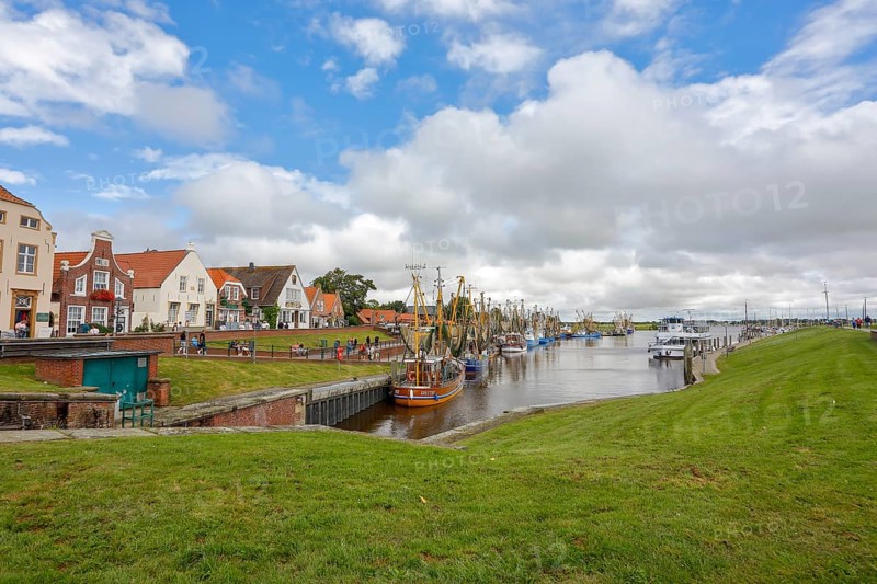 View of historic houses with colourful facades at the old harbour of Greetsiel, with fishing boat, under blue sky, Greetsiel, East Frisia, Lower Saxony, Germany, Europe