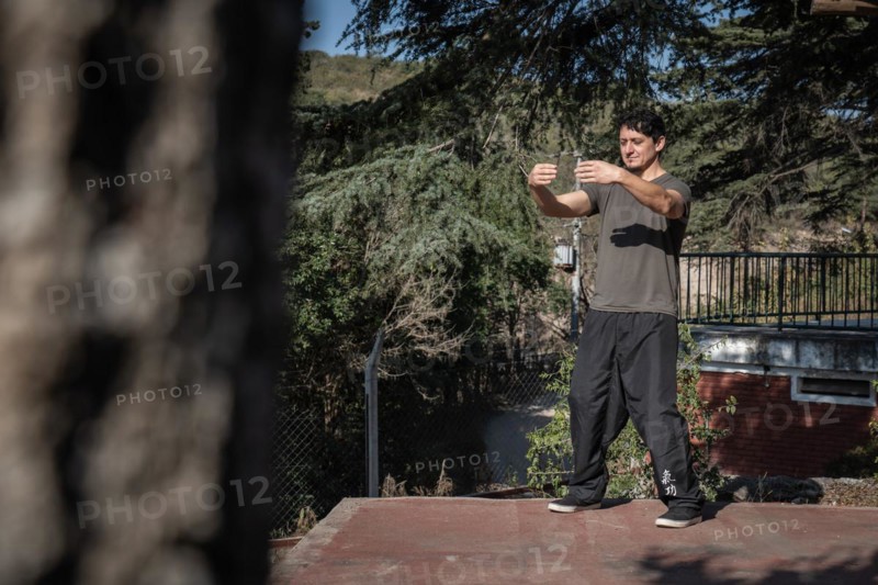 Distant view of a focused man practicing Chi Kung with his eyes closed in the Tree Hugging posture