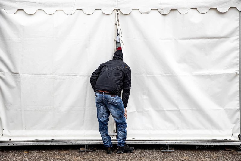 Curiosity, curious man, sticks his head into an event tent, through a gap and watches from outside