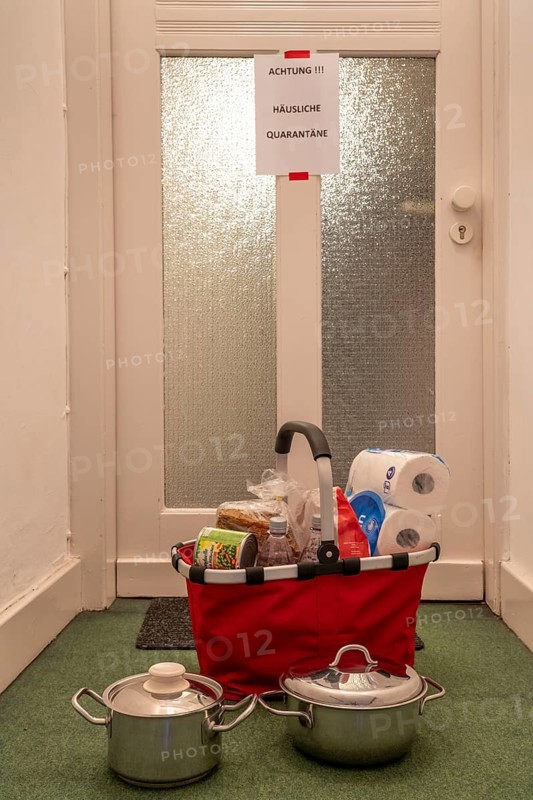 Symbolic image Domestic quarantine, man is in isolation at home due to a suspected corona infection, warning sign for visitors on the front door, communicates with a visitor through the door, neighbours have been shopping, cooked and put the things in front of the door
