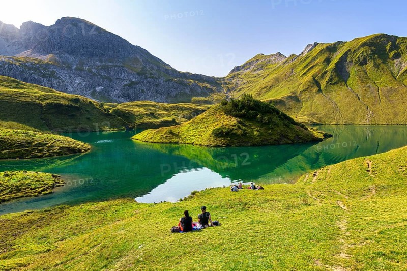 People sit in a meadow at the Schrecksee and enjoy a picnic in front of a picturesque mountain and lake landscape, Allgäu Alps, Bad Hindelang, Allgäu, Bavaria, Germany, Europe