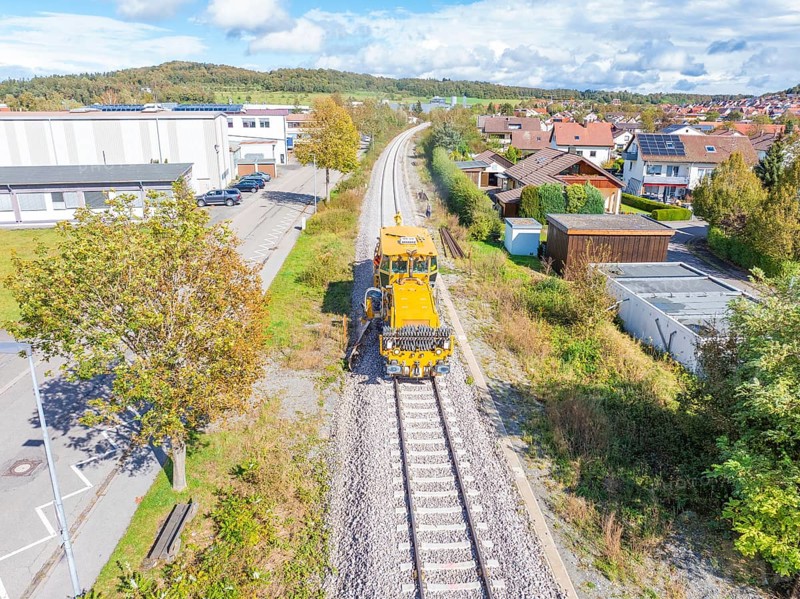 Yellow maintenance vehicle on the tracks, surrounded by trees and residential buildings with a factory nearby, tamping machine, Hermann Hessebahn, Althengstett, Black Forest, Germany, Europe