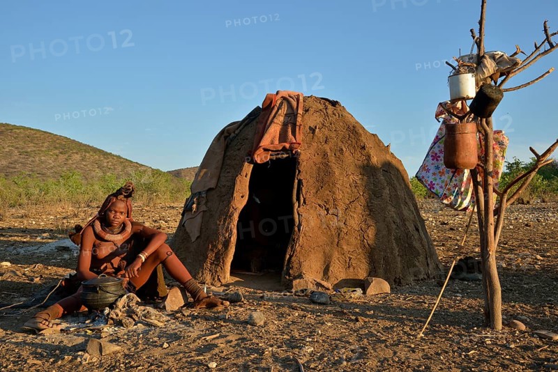 Young Himba woman sitting at a campfire in front of her hut, Ombombo, Kaokoland, Kunene, Namibia, Africa