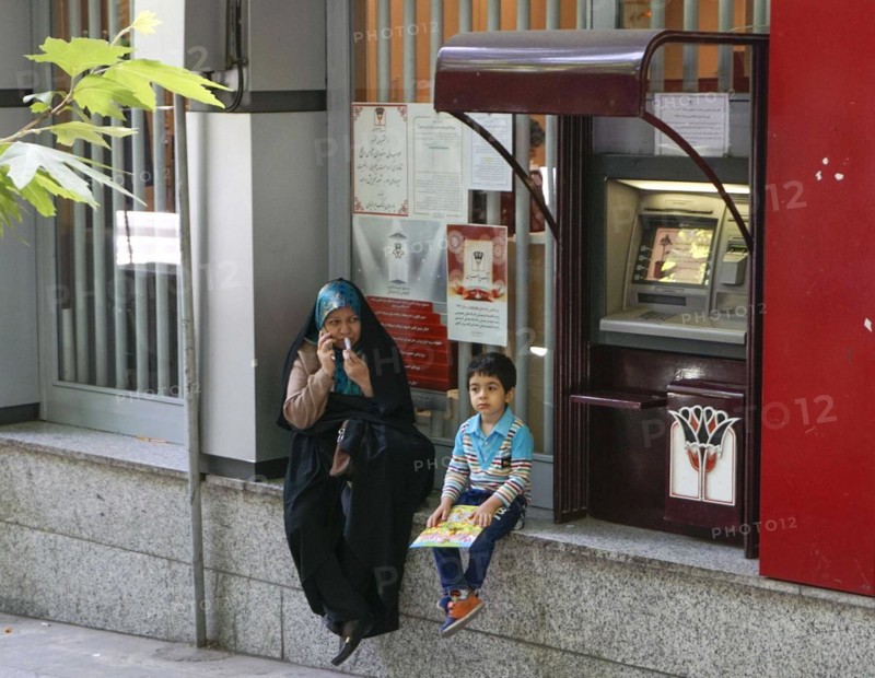 A mother sits with her child next to an ATM in Tehran, 17/05/2016