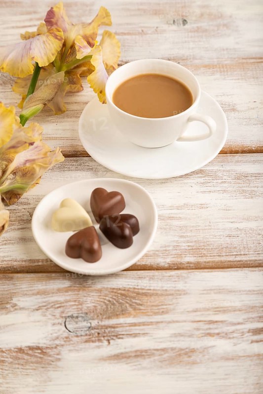 Cup of cioffee with chocolate candies, lilac and purple iris flowers on white wooden background. side view, flat lay, close up, still life. Breakfast, morning, spring concept