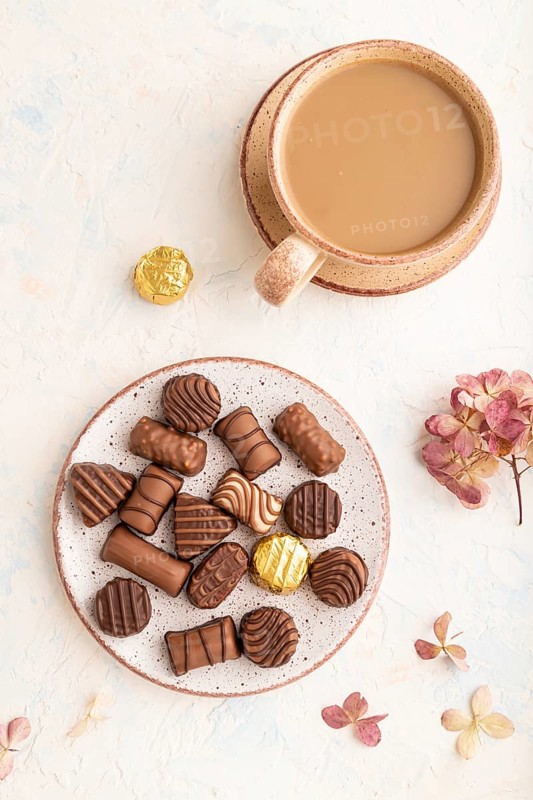 Chocolate candies with cup of coffee and hydrangea flowers on a white concrete background. top view, flat lay, close up