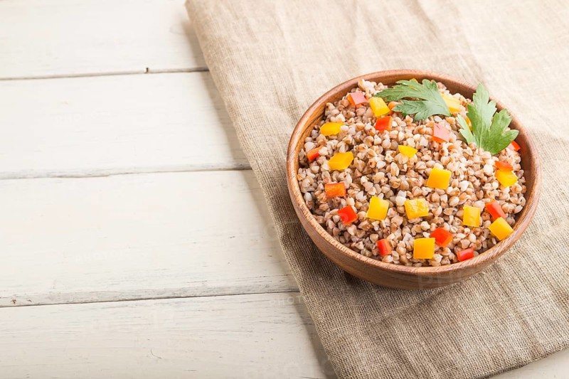 Buckwheat porridge with vegetables in wooden bowl on a white wooden background and linen textile. Side view, copy space, selective focus. Russian traditional cuisine