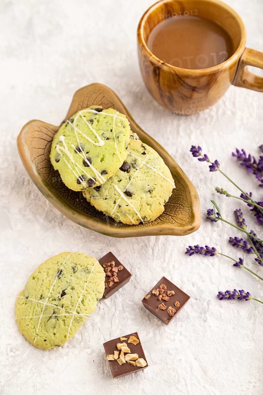 Green cookies with chocolate and mint on leaflike ceramic plate with cup of coffee on gray concrete background. side view, close up, selective focus