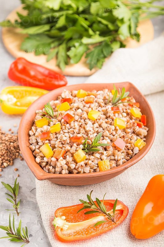 Buckwheat porridge with vegetables in clay bowl on a gray concrete background and linen textile. Side view, selective focus, close up. Russian traditional cuisine