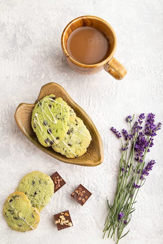 Green cookies with chocolate and mint on leaflike ceramic plate with cup of coffee on gray concrete background. top view, flat lay, close up