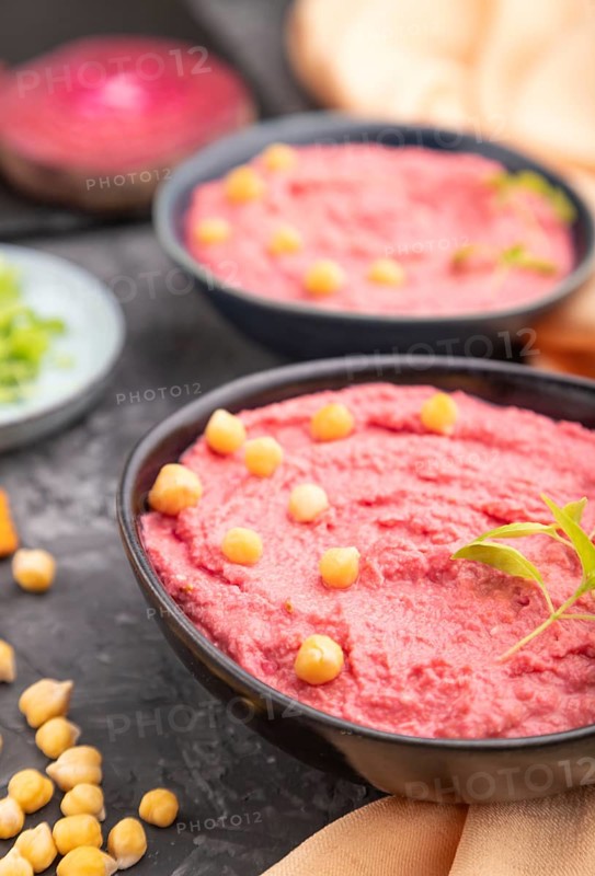 Hummus with beet and microgreen basil sprouts in ceramic bowl on a black concrete background and orange textile. Side view, close up, selective focus