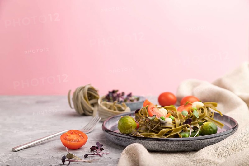 Tagliatelle green spinach pasta with tomato, pea and microgreen sprouts on a gray and pink background and linen textile. Side view, copy space, selective focus