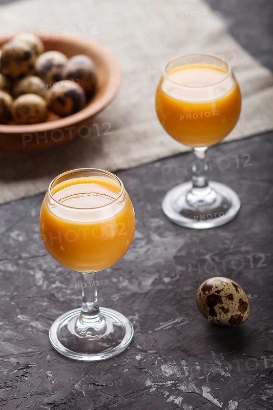 Sweet egg liqueur in glass with quail eggs on a black concrete background. Side view, low key, close up