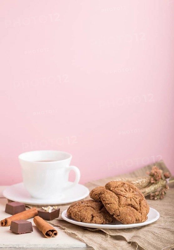 Homemade oatmeal cookies with a cup of cocoa on a linen textile and pink pastel background. side view, close up, selective focus, copy space