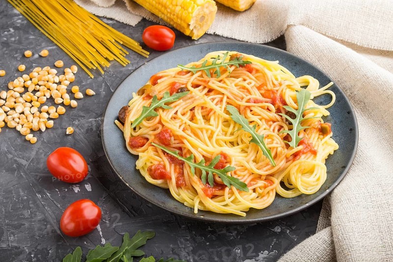 Corn noodles with tomato sauce and arugula on a black concrete background and linen textile. Side view, close up