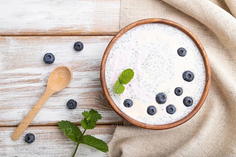 Yogurt with blueberry in wooden bowl on white wooden background and linen textile. top view, flat lay, close up