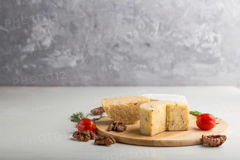 Cheddar and various types of cheese with rosemary and tomatoes on wooden board on a gray and white background. Side view, copy space, selective focus