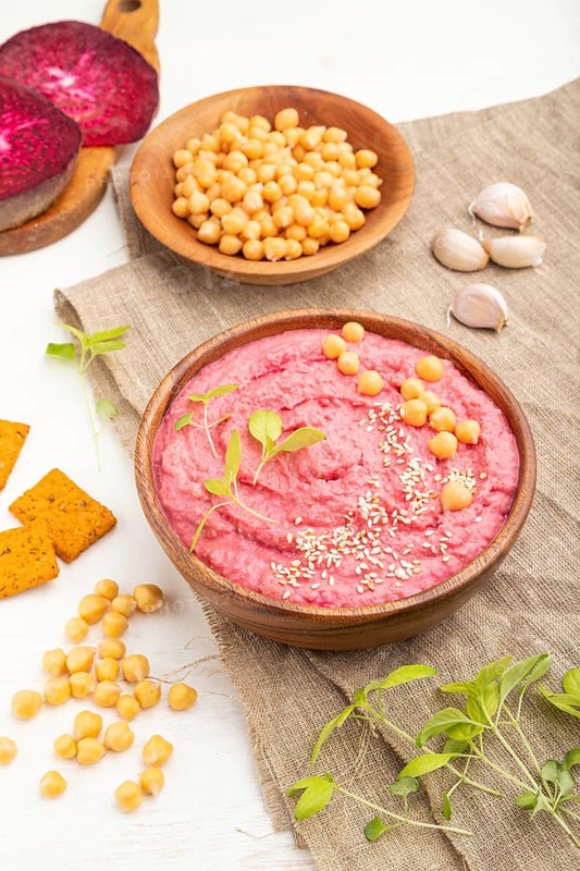 Hummus with beet and microgreen basil sprouts in wooden bowl on a white wooden background and linen textile. Side view, close up