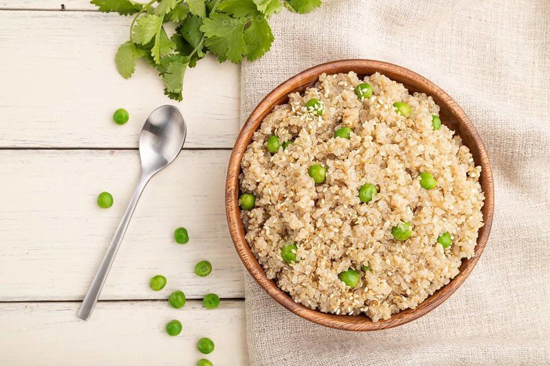 Quinoa porridge with green pea in wooden bowl on a white wooden background and linen textile. Top view, flat lay, close up