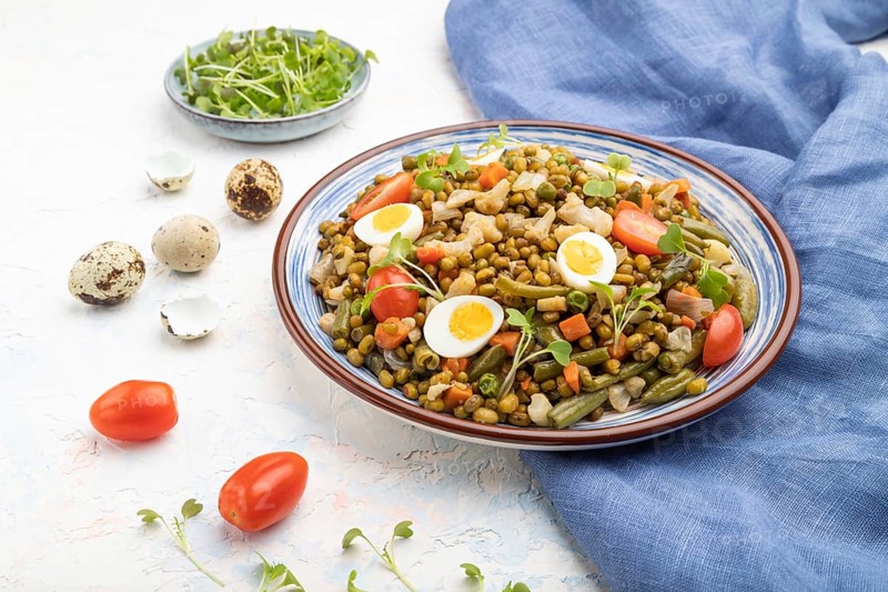 Mung bean porridge with quail eggs, tomatoes and microgreen sprouts on a white concrete background and blue textile. Side view, close up