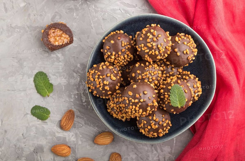 Chocolate caramel ball candies with almonds and a cup of coffee on a gray concrete background and red textile. top view, flat lay, close up