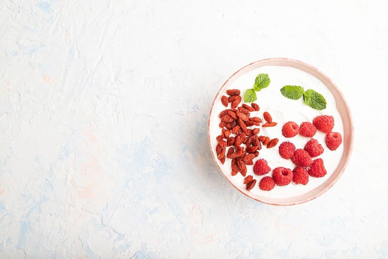 Yogurt with raspberry and goji berries in ceramic bowl on white concrete background. top view, flat lay, copy space