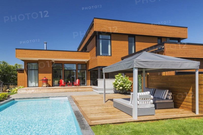 Rear of modern cube style home with stained horizontal wood cladding, in-ground swimming pool and wooden deck with grey gazebo canopy, Quebec, Canada, North America