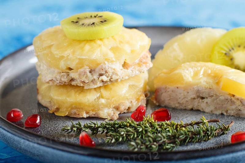 Pieces of baked pork with pineapple, cheese and kiwi on gray plate and blue background, side view, close up, selective focus