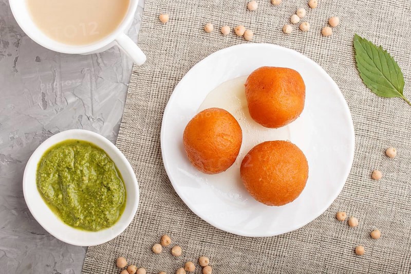 Traditional indian candy gulab jamun in white plate with mint chutney on a gray concrete background. top view, flat lay. close up