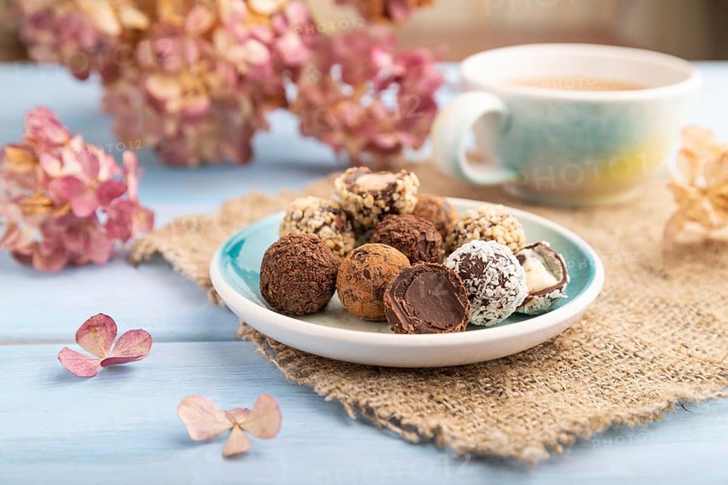 Chocolate truffle candies with cup of coffee on a blue wooden background and linen textile. side view, close up, selective focus