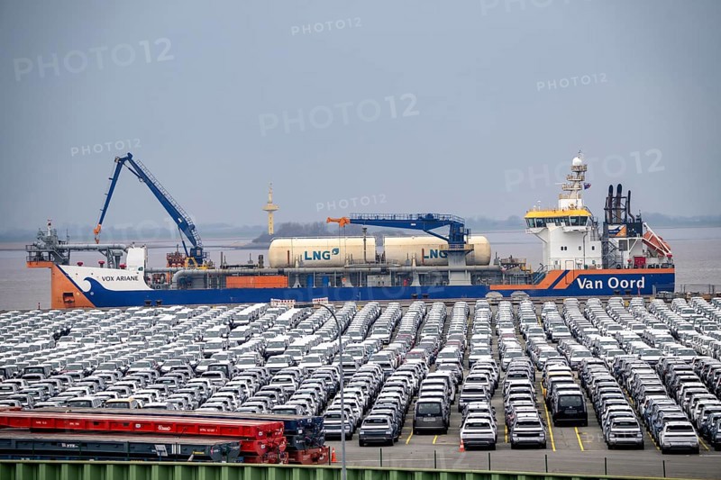 Parking space for import vehicles, hundreds of Hyundai Ioniq, electric cars, waiting for onward transport, behind them, on the Weser, the dredger, the hopper dredger, suction dredger, Vox Ariane, which holds the tug to a certain depth, at the EUROGATE container terminal in the overseas port of Bremerhaven, Lower Saxony, Germany, Europe