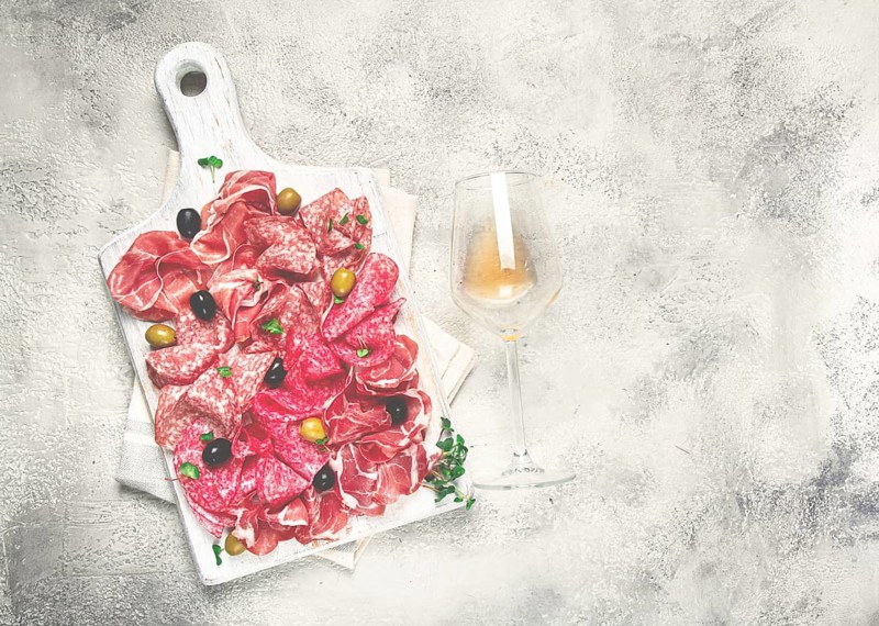 Assorted, meat appetizer, prosciutto, salami and ham, with olives, on a wooden white board, light background, breakfast, top view, close-up, no people