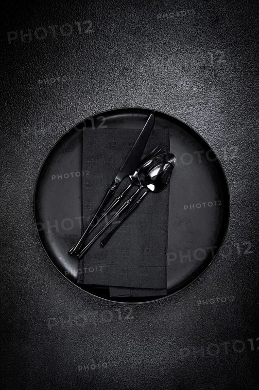 Food background, with an empty black plate, black cutlery, with a napkin, on a black background, table setting, top view, no people